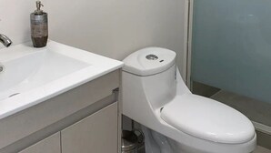 Une salle de bain avec des toilettes blanches, un lavabo et une douche à parois de verre.