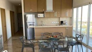Une cuisine moderne dotée d’un îlot central, d’appareils électroménagers en acier inoxydable et d’un coin repas avec une table et des chaises en verre.