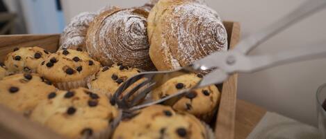 A wooden tray containing various baked goods, including muffins and a pastry dusted with powdered sugar.