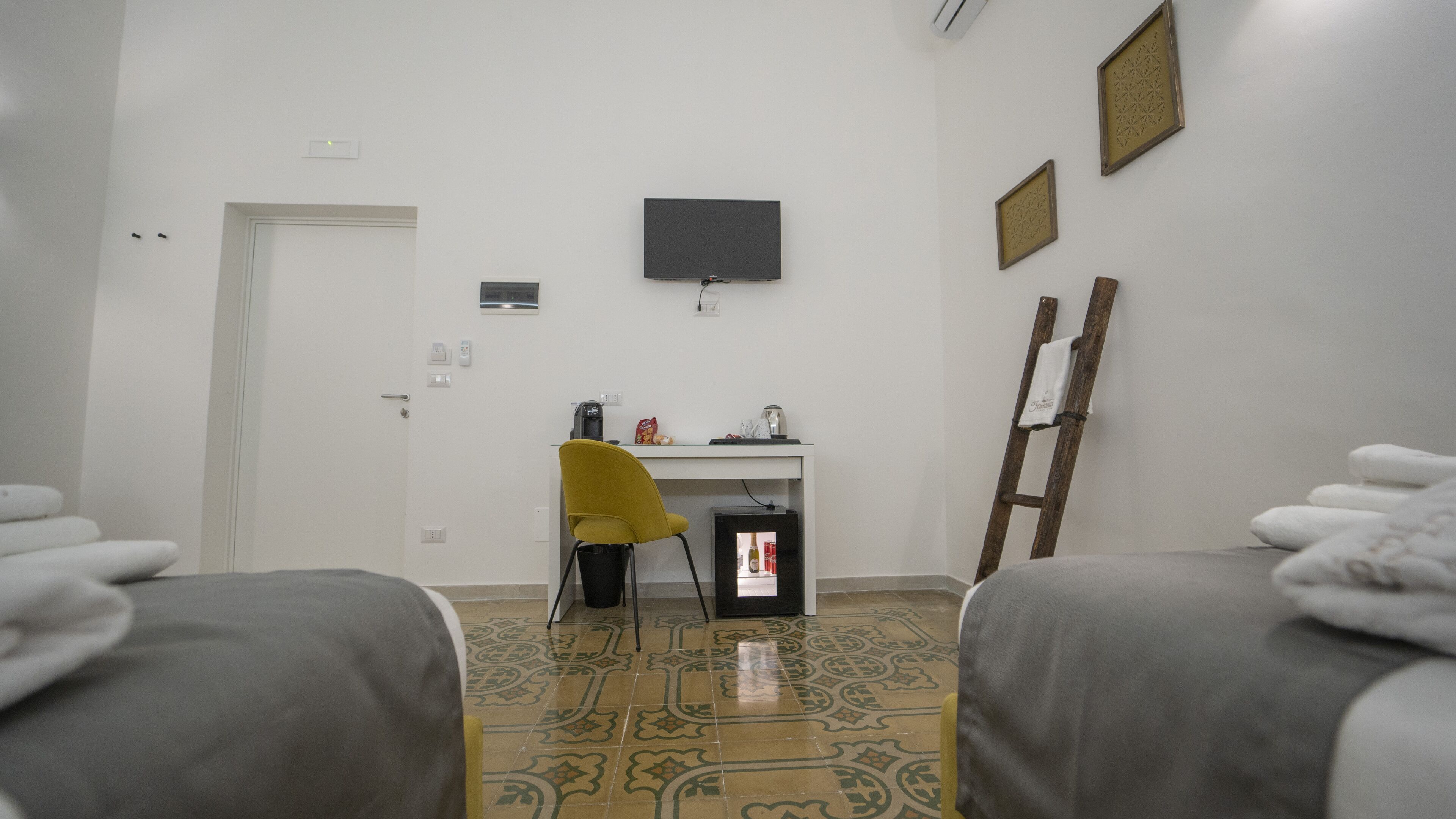 A hotel room with two beds, a desk with a chair, a television, and a small refrigerator.