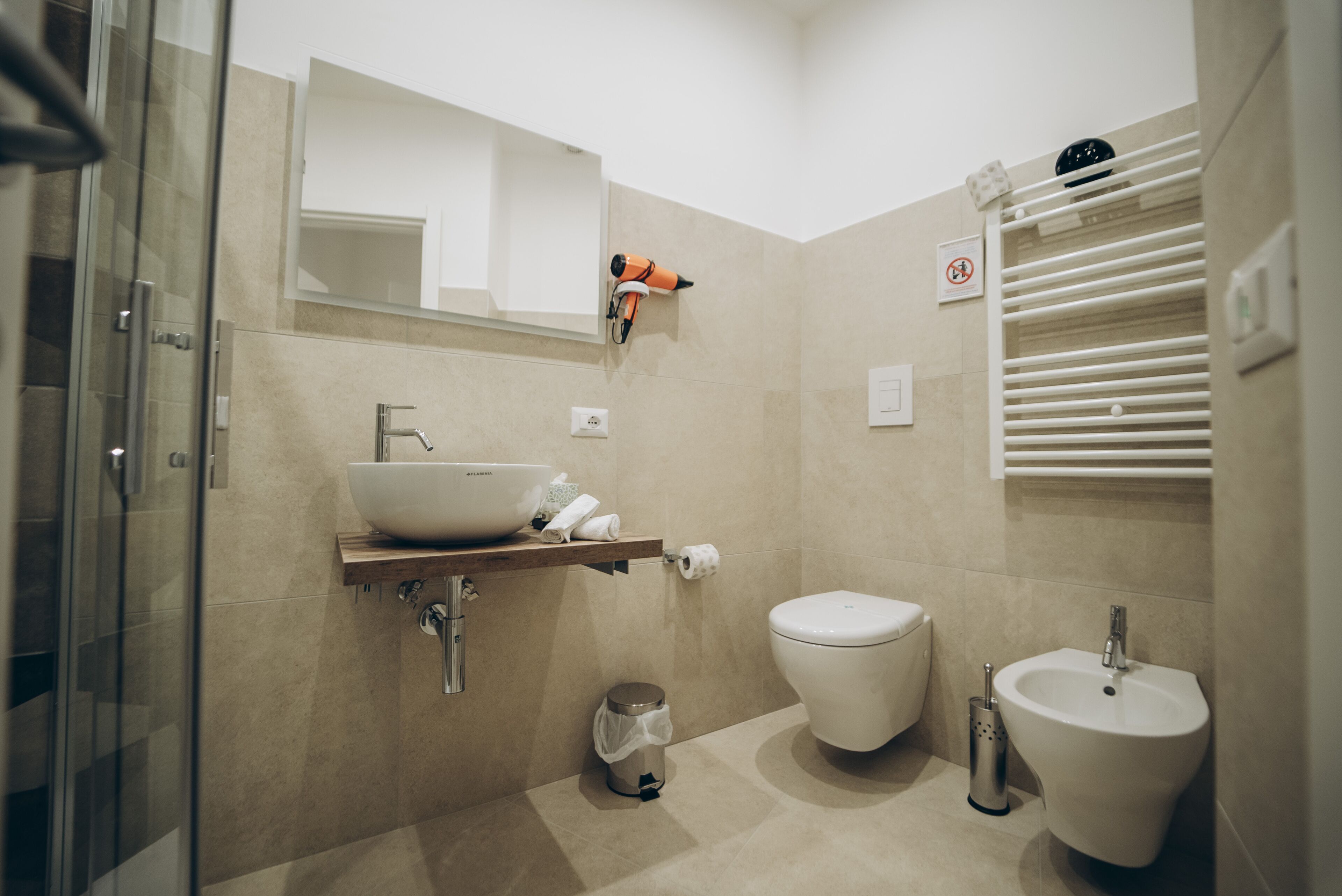 A modern bathroom with a glass shower enclosure, a white sink, a bidet, and a toilet.