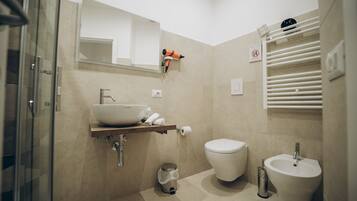 A modern bathroom with a glass shower enclosure, a white sink, a bidet, and a toilet.