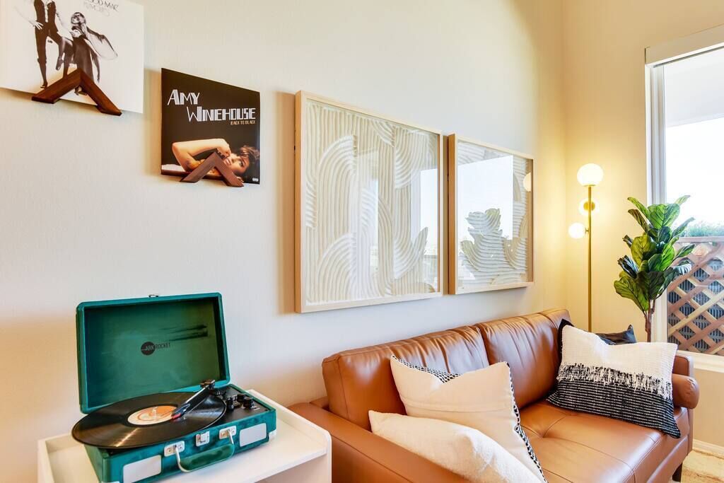 A living room with a brown leather sofa, a teal record player, and framed artwork on the wall.