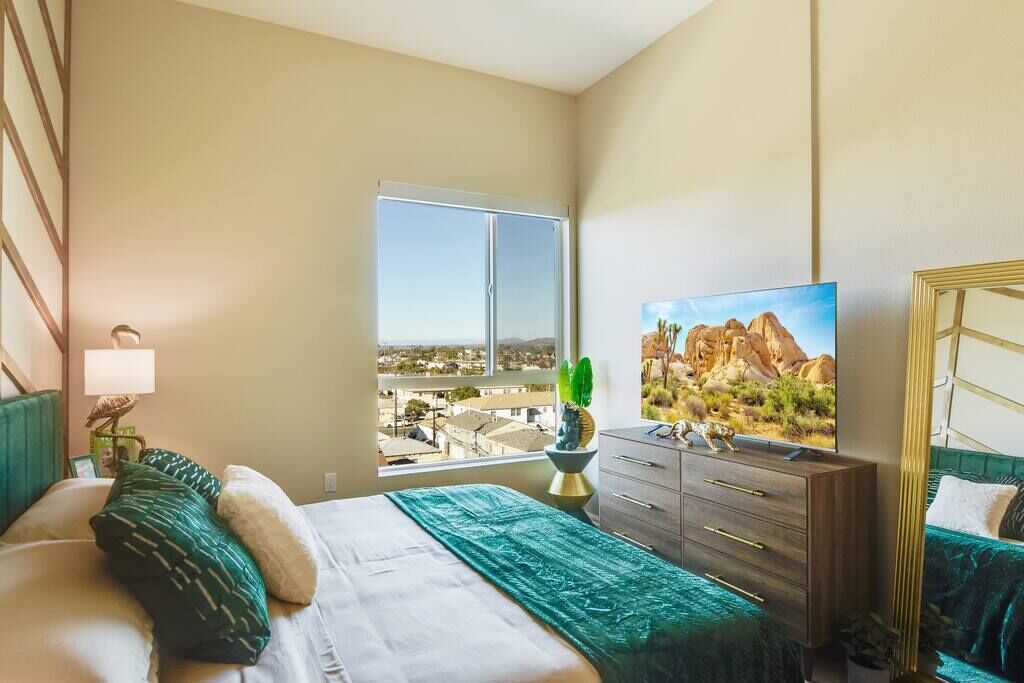 A hotel room with a bed, a dresser, a television, and a window with a city view.