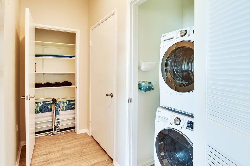 A laundry room with two stacked washing machines, a drying rack, and a storage cabinet.