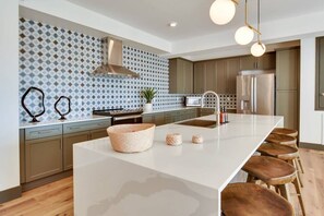 Une cuisine moderne dotée d’un îlot central, de tabourets de bar, d’un réfrigérateur en acier inoxydable et d’un pare-feu décoratif.