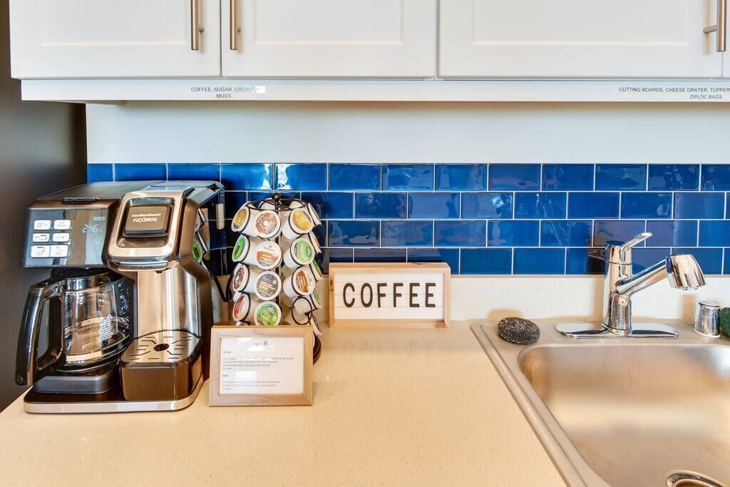 A kitchen counter with a coffee maker, a coffee grinder, a coffee-themed decorative item, and a 'COFFEE' sign.