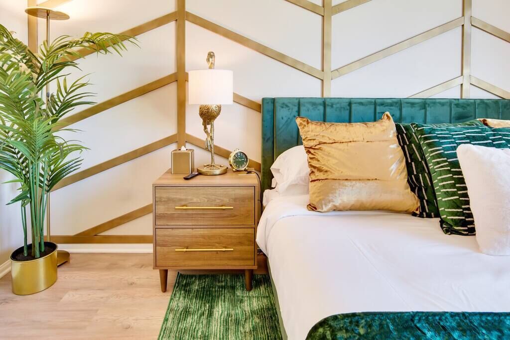 A bedroom with a bed, bedside table, lamp, and a potted plant.