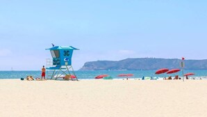 A lifeguard tower labeled '3C' on a beach with red umbrellas and people sunbathing.