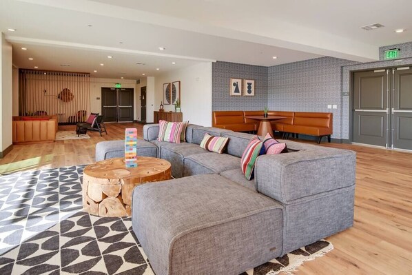 A modern lobby with a grey sectional sofa, a wooden coffee table, and a patterned rug.