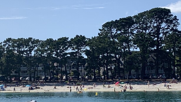 En strand med folk, en båt och en rad hus i bakgrunden.