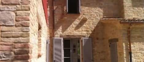Un edificio de piedra con un ventanal pequeño y una puerta con contraventanas.