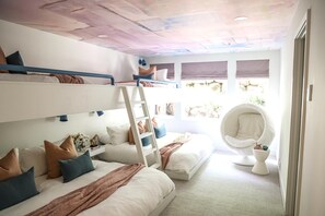 Habitación tipo dormitorio con literas, una escalera, un sillón colgante y una ventana con vistas al exterior.