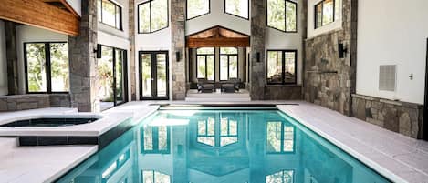 A large indoor swimming pool with stone walls and wooden beams, surrounded by large windows.