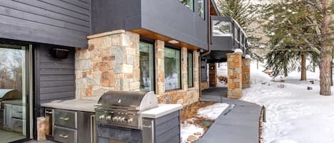 Una casa moderna con facciata in pietra, ampie finestre e barbecue integrato all'esterno.