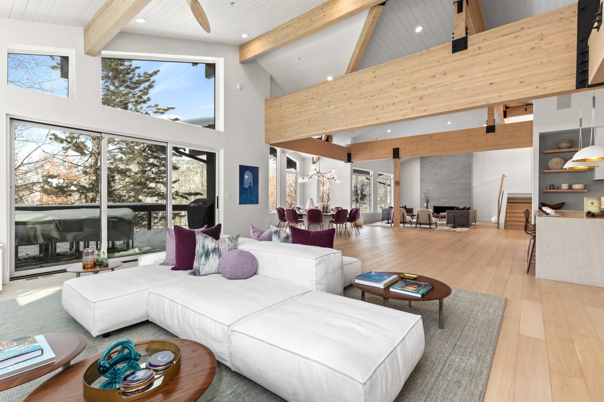 A spacious living area with a large white sectional sofa, a dining table with chairs, and a fireplace.