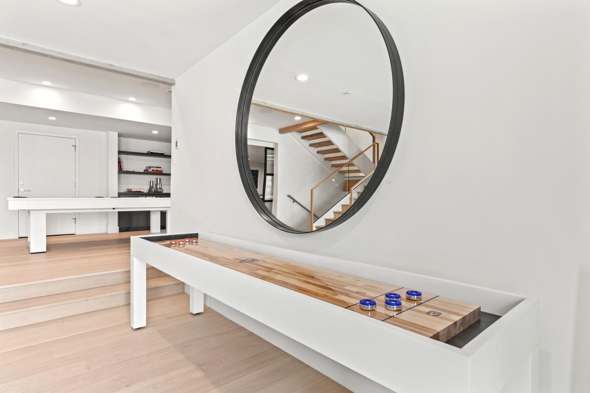 Un interior moderno con un banco blanco, un espejo redondo y una mesa de madera con objetos azules.