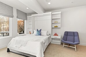 Un dormitorio moderno con una cama, estanterías integradas, una silla y una ventana con vistas a árboles.