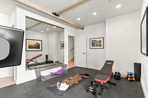 Un gimnasio moderno en casa con barra de dominadas, prensa de pesas, mancuernas y una colchoneta para yoga.