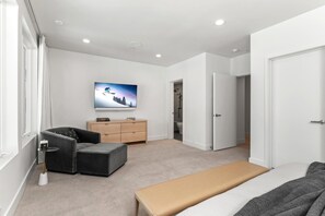 A modern bedroom with a bed, a bench, a TV, a dresser, and a door leading to another room. - Park City | KBM Resorts | Indoor Pool,Home Theater, Playground | Single Unit, 6 Bedrooms |  ML-618 (Park City)