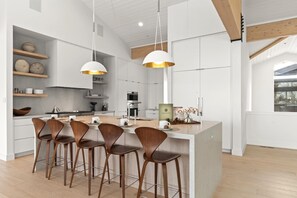 Una cocina moderna con una isla central, taburetes de bar, iluminación colgante y vigas de madera.