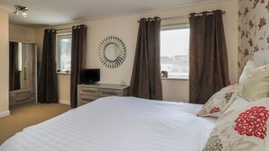 A bedroom with a bed, a dresser, a television, and a window with curtains. - The Heights (Windermere)