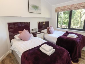 Une chambre d’hôtel avec deux lits, une table de chevet, un miroir et une fenêtre donnant sur des arbres.