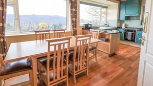 Un espace repas avec une table et des chaises en bois, une cuisine aux armoires de couleur turquoise et de grandes fenêtres offrant une vue sur l’extérieur.
