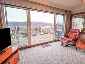 A spacious balcony with a view of hills, a red leather chair, and a wooden dresser with a flat-screen TV. - Tanna Hill (Windermere)