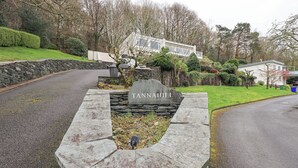 Une plaque de pierre portant le nom « Tannagh Hill », située dans un espace aménagé avec une route, un mur de pierres et des immeubles résidentiels en arrière-plan.