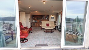 Un balcon spacieux doté d’un sol à carreaux, un coin salon avec un canapé et des fauteuils, et une bibliothèque.