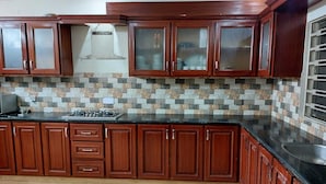 A kitchen with wooden cabinets, a tiled backsplash, and a black countertop. - Beautiful 3-bed House in Islamabad (Rawalpindi)