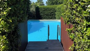 Una terraza de madera que conduce a una piscina azul cristalina rodeada de abundante vegetación.