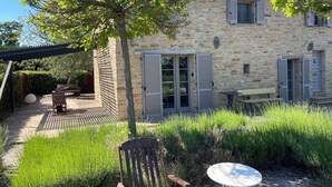 Una casa de piedra con persianas, un patio con mesa y sillas, y un jardín.