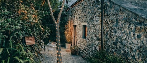 A stone building with a gravel path, a palm tree, and string lights.