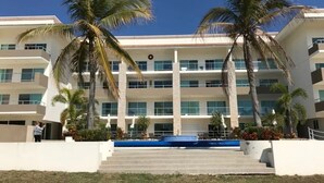 A multi-story hotel with a central courtyard, palm trees, and a swimming pool. - Condos SB (Mazatlán)