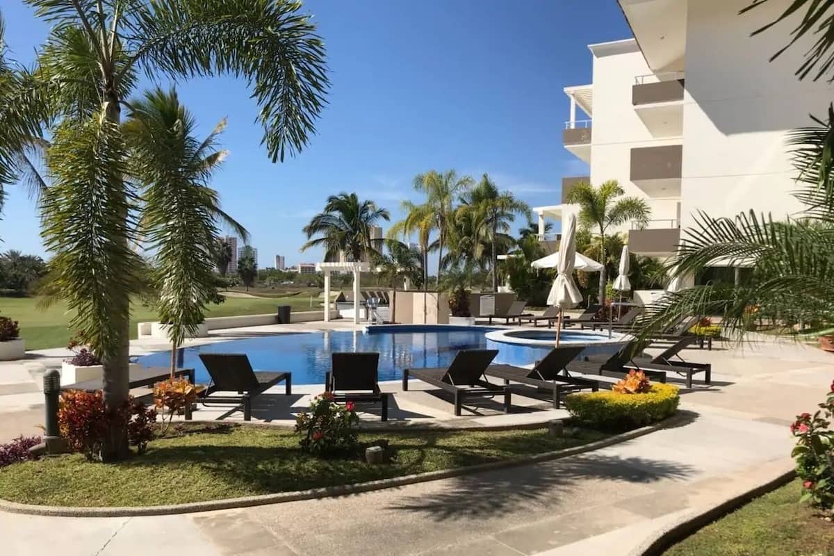 Un área de piscina con sillones de descanso y palmeras.