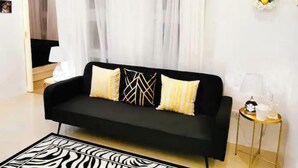 Un sofá negro con cojines estampados, un felpudo a rayas de cebra y una pequeña mesa redonda con una lámpara y objetos decorativos.