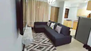 Una sala de estar moderna con un sofá de color oscuro, una alfombra estampada y un televisor montado en la pared.