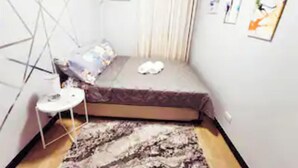 Un dormitorio pequeño y ordenado con cama, una mesita y una alfombra.