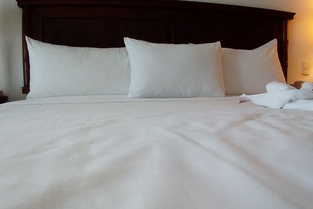 A neatly made bed with white linens and pillows, a wooden headboard, and a visible wall switch.
