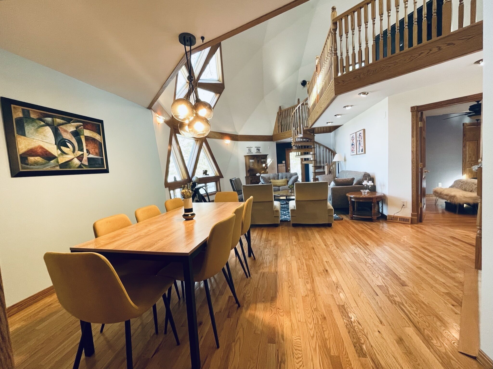 Un vaste espace dédié à la salle à manger, avec une table et des chaises en bois, un escalier menant à un niveau supérieur et une grande fenêtre qui laisse entrer la lumière naturelle.