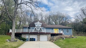 A two-story house with a front deck, garage, and a stone foundation. - Dome House on Whitewater Lake (Whitewater)