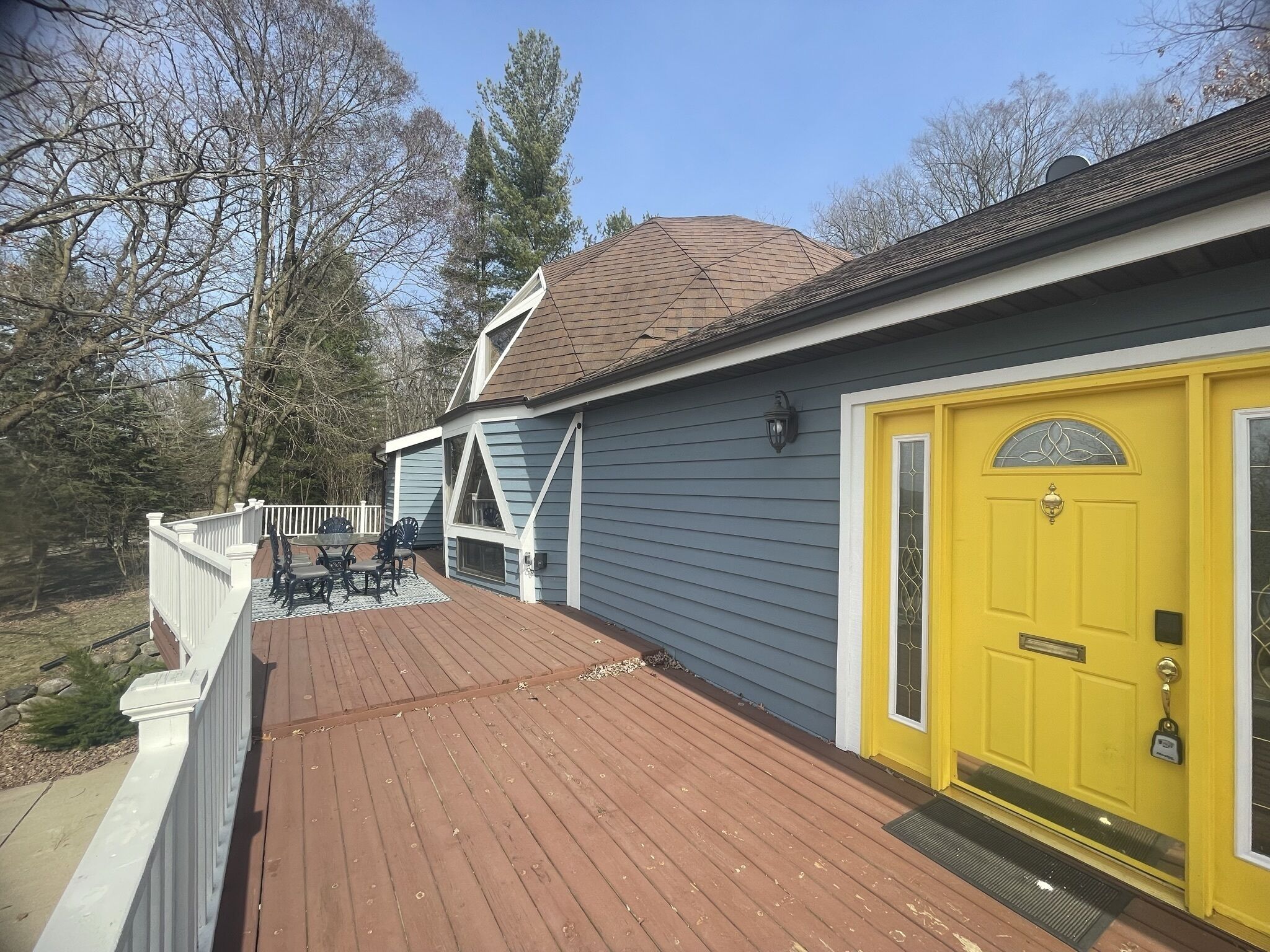 A house with a yellow front door, a deck, and a fenced patio area.