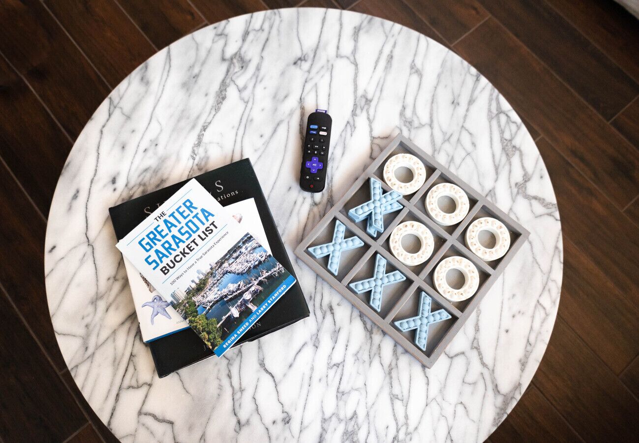 Ein Buch mit dem Titel „The Great Sarasota Bucket List“ und ein Tic-Tac-Toe-Spiel auf einem Marmortisch.