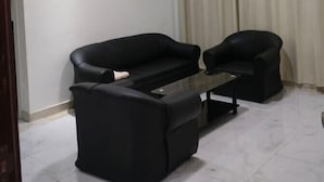Une pièce avec un canapé noir, une petite table basse et une fenêtre ornée de rideaux beiges.