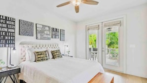 Une chambre à coucher comprenant un lit, un ventilateur de plafond, une table de chevet, une lampe et une vue sur l’extérieur grâce à une porte coulissante.