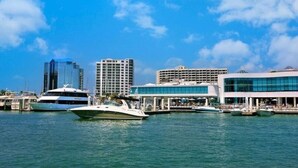 Un port de plaisance où sont amarrés plusieurs yachts, des bâtiments modernes et un ciel d’un bleu éclatant.