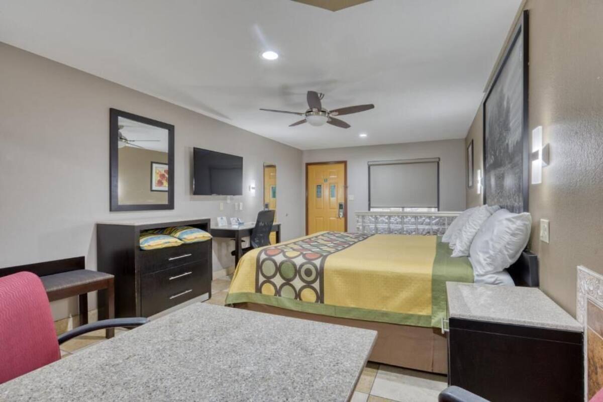 A hotel room with a bed, desk, chair, wardrobe, and a ceiling fan.