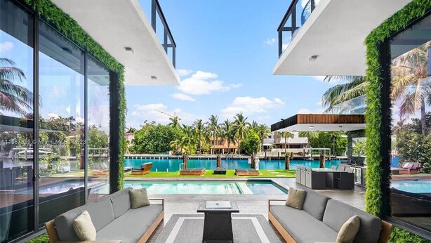 A modern outdoor lounge area with a pool, two sofas, and a coffee table, overlooking a pool and greenery. - Playa Villa - Modern Luxury Redefined (Miami Beach)